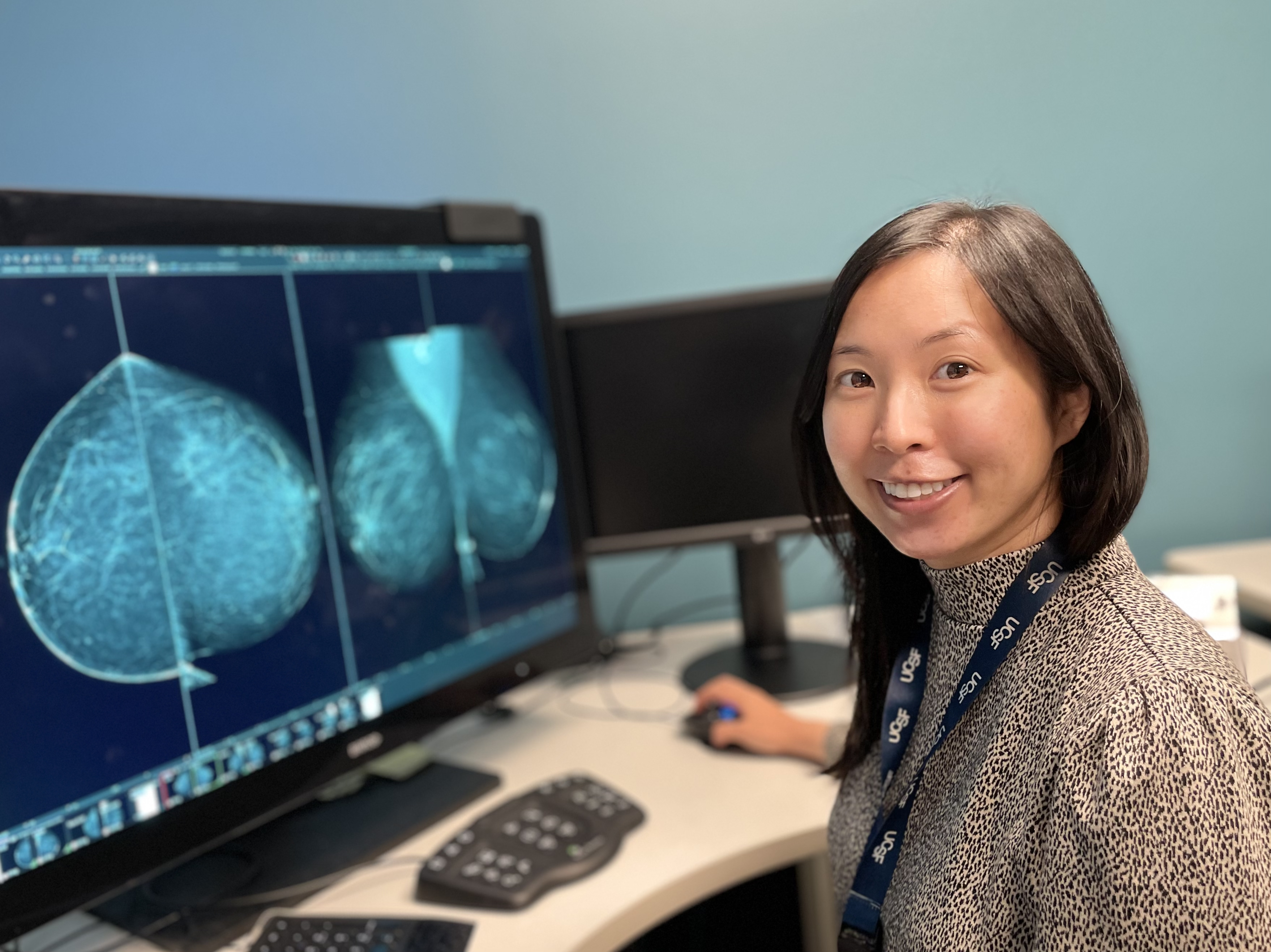 Maggie Chung, MD. A woman smiling as she sits at a computer workstation.