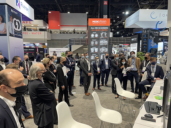 The AI Imaging in Practice demonstration in action A group standing around a display listening to a demonstration at a conference