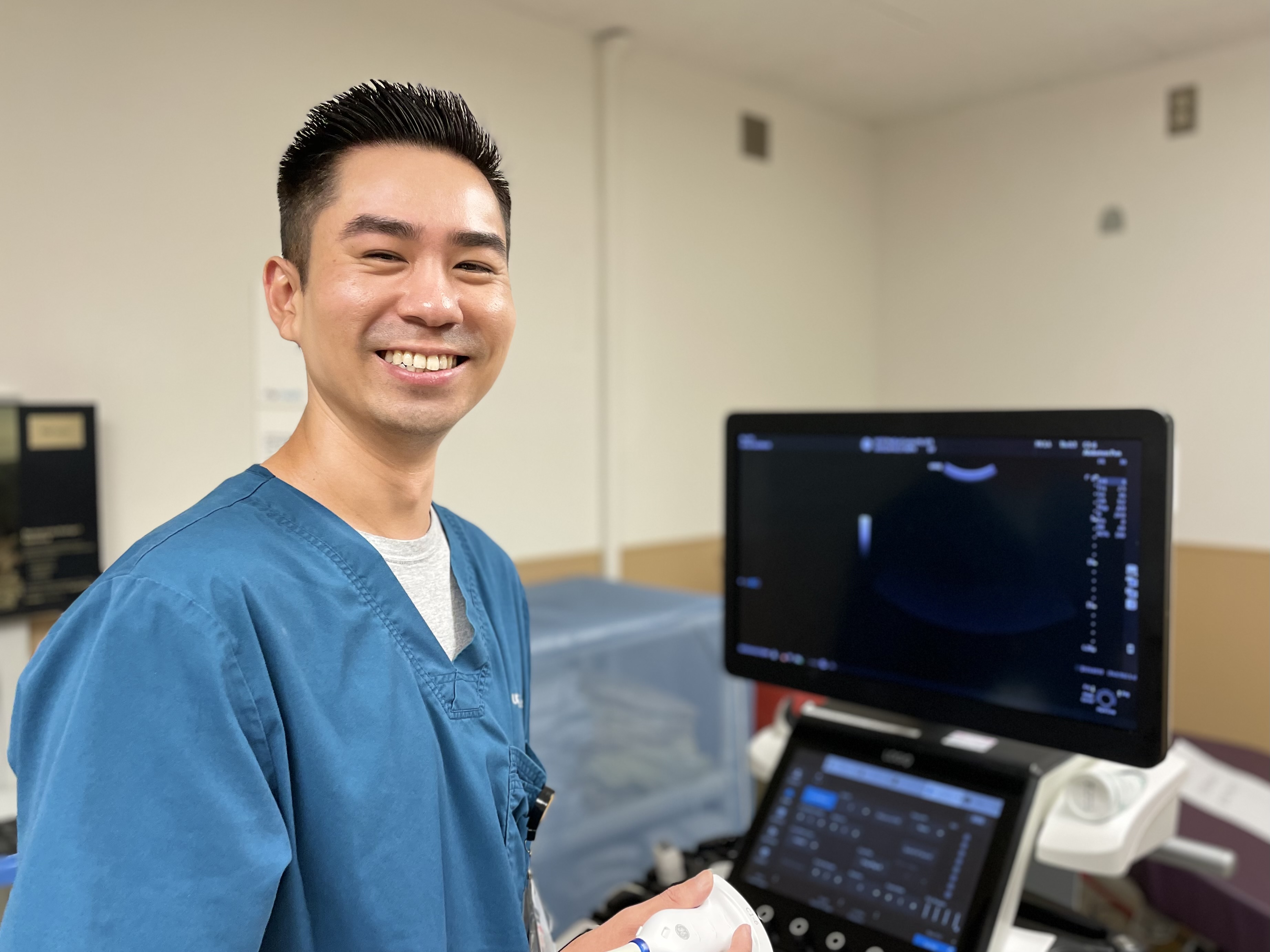 Brent Yim, RDMS, Senior Ultrasound Technologist, Parnassus Heights. Man smiling in front of ultrasound machine.