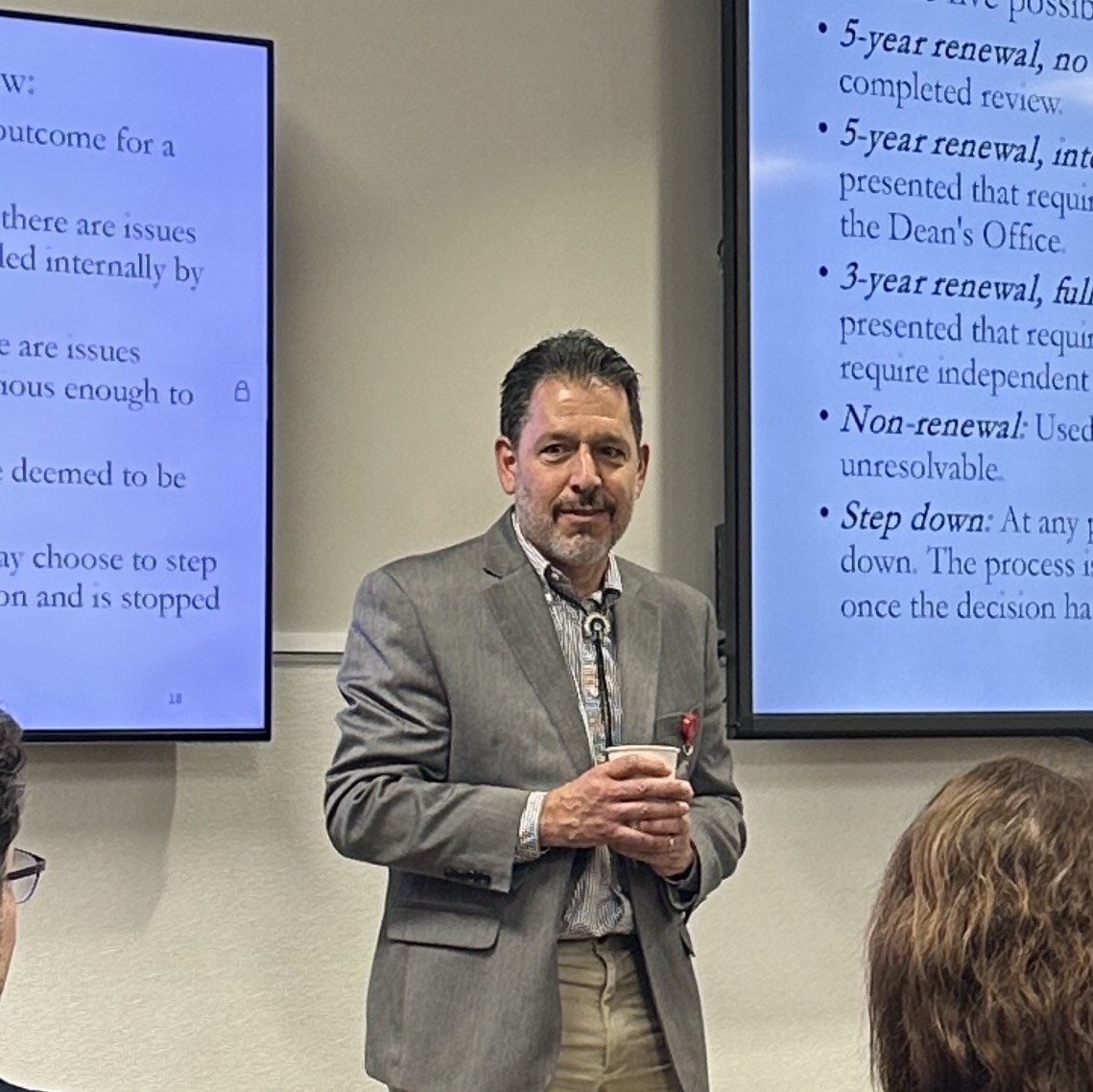 Man in a suit standing in front of screens