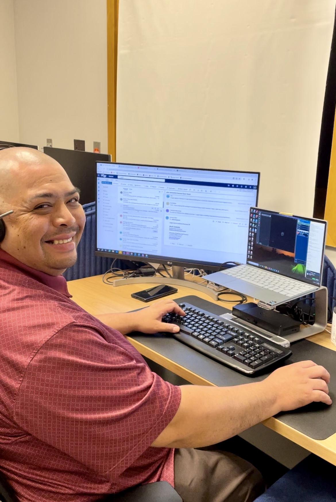 Man at a computer with a headset on smiling.