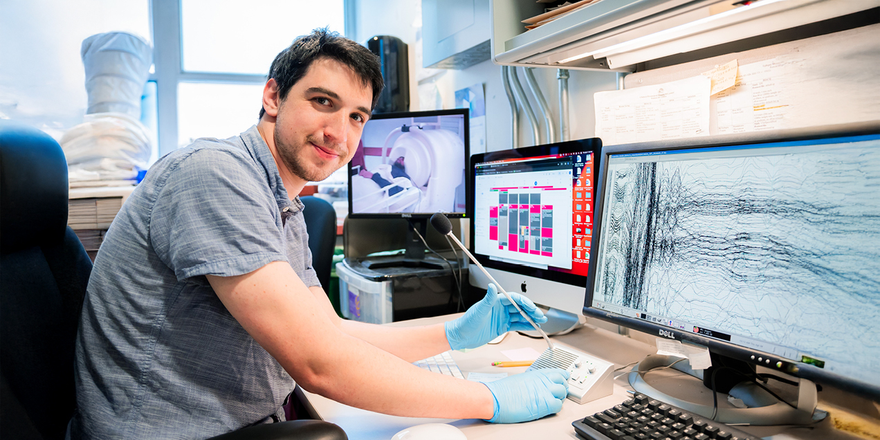 Researcher analyzing quantitative imaging data at a workstation, with MRI scans and signal plots displayed on multiple computer monitors in a lab setting.