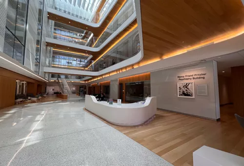 Bright, multi-story atrium of the Nancy Friend Pritzker Psychiatry Building with a central reception desk, wood finishes, and glass-lined upper floors.