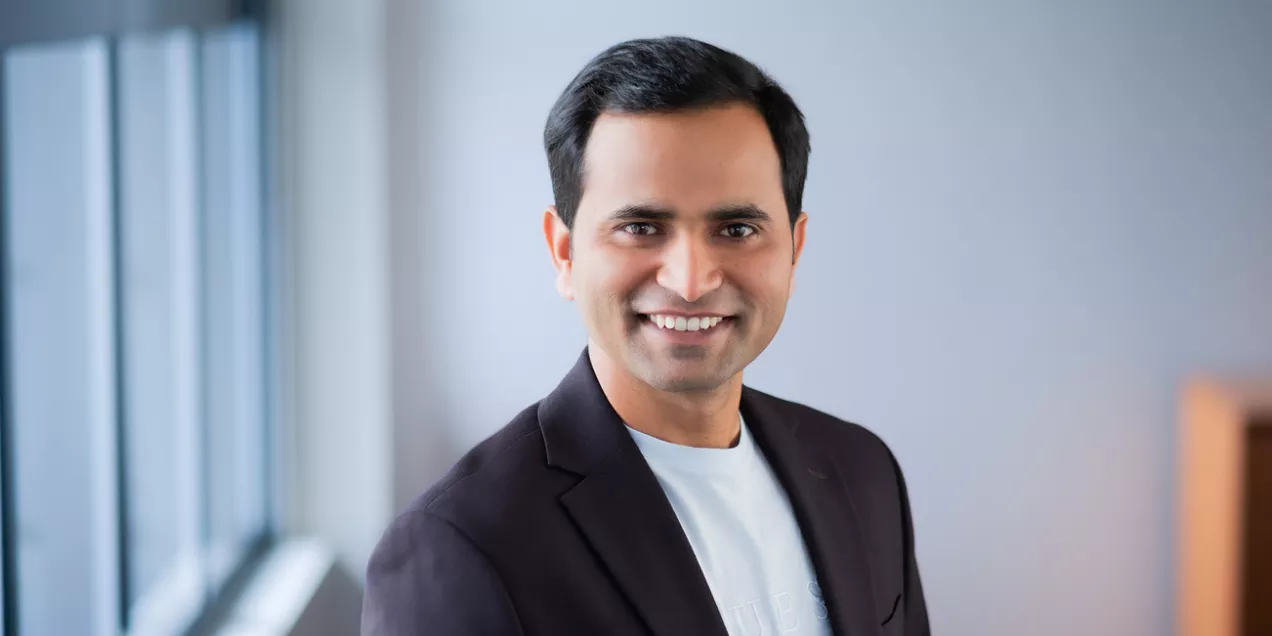 Anil Bidkar smiling, wearing a dark blazer and light shirt, standing near a window with a blurred background. The UCSF logo appears on the right against a dark blue backdrop.