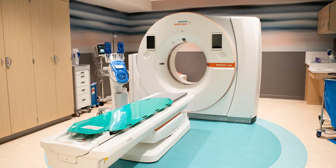 A CT scan room featuring a Siemens SOMATOM X.cite scanner with the patient table extended, surrounded by medical equipment and storage cabinets in a clean, modern clinical setting.
