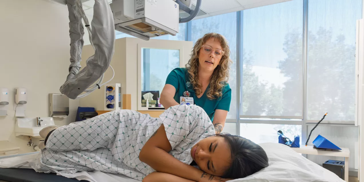 A clinician and a patient interact in a clinical exam room at the Orthopedic Institute, with medical equipment visible nearby.