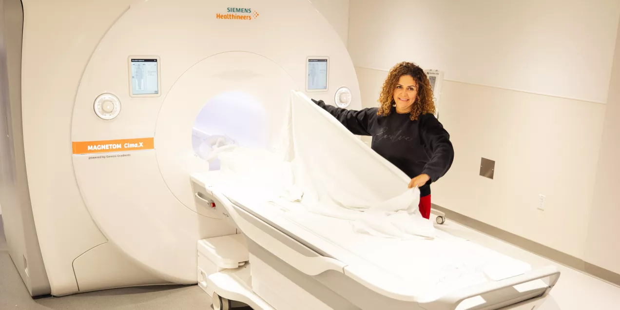 A clinician prepares an MRI table in a scanning room, standing beside a Siemens MRI machine.