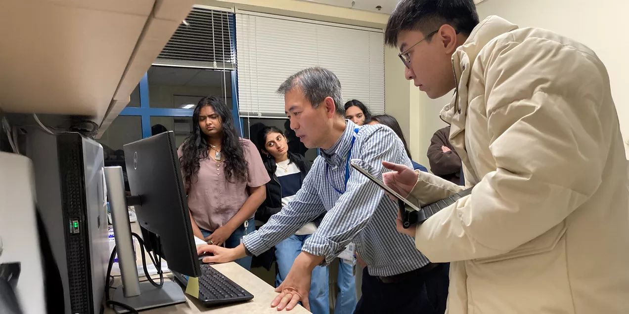 Faculty member demonstrates imaging software on a desktop computer while a group of students observe closely in a classroom lab setting.