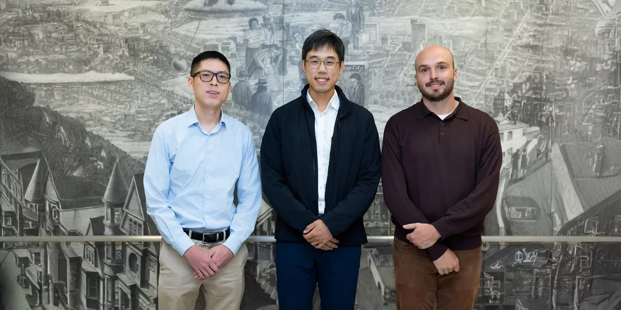 Three cardiothoracic imaging fellows standing side by side in front of a detailed grayscale mural, wearing business-casual attire and smiling toward the camera.
