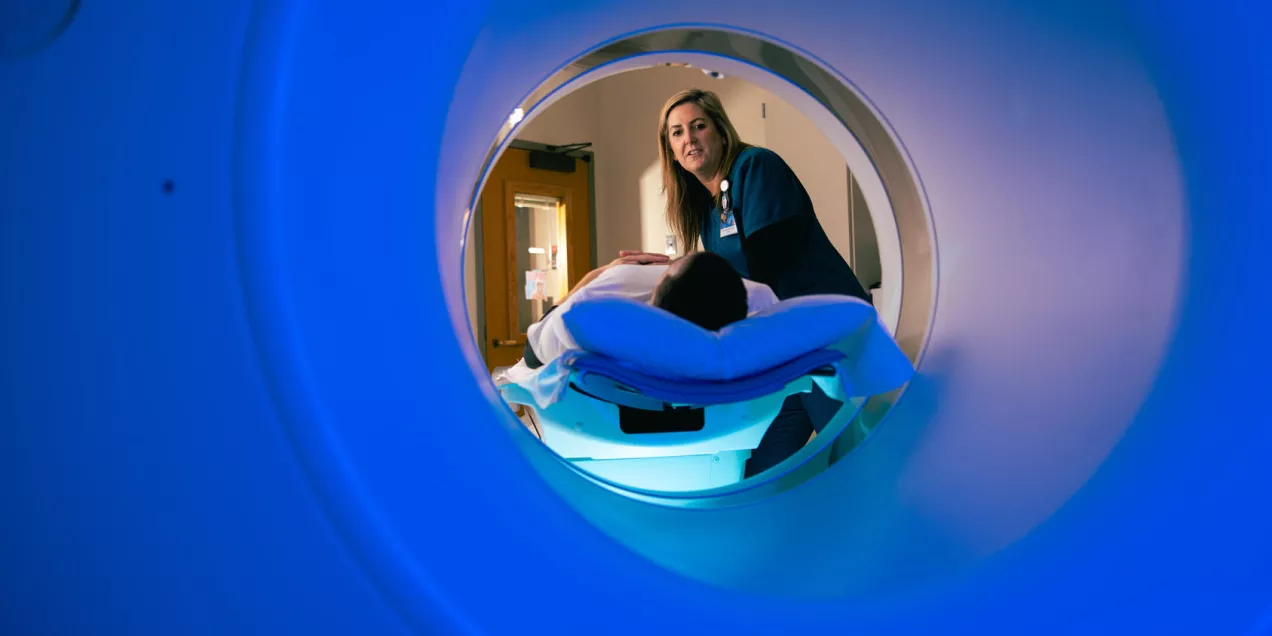 Radiologic technologist positioning a patient on a CT scanner table, viewed from inside the scanner ring.
