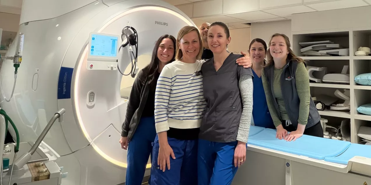Group of clinical staff standing beside an MRI scanner in a hospital imaging room