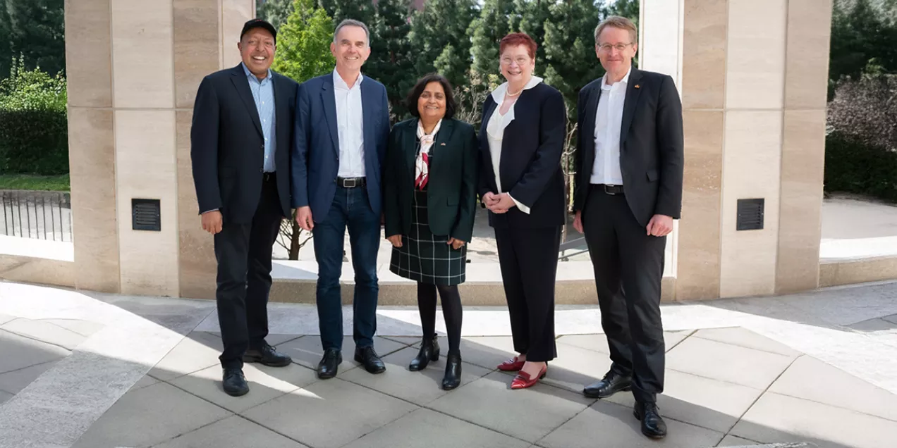 Five professionally dressed individuals stand together outdoors between stone columns, smiling at the camera during the AI Exchange 2024 event.