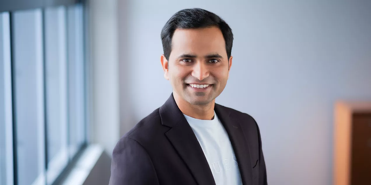 Professional portrait of Anil Bidkar, PhD, smiling and standing indoors near a window while wearing a dark blazer over a light-colored shirt.