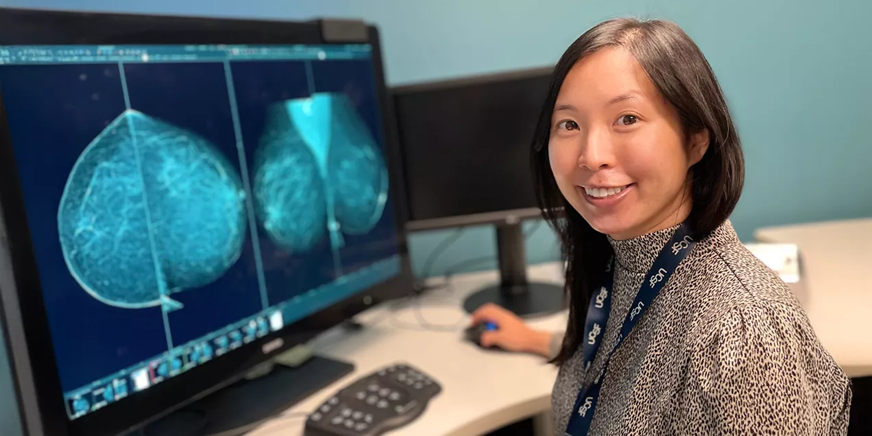 Healthcare professional seated at a workstation reviewing mammogram images displayed on a computer monitor in a breast imaging reading room.