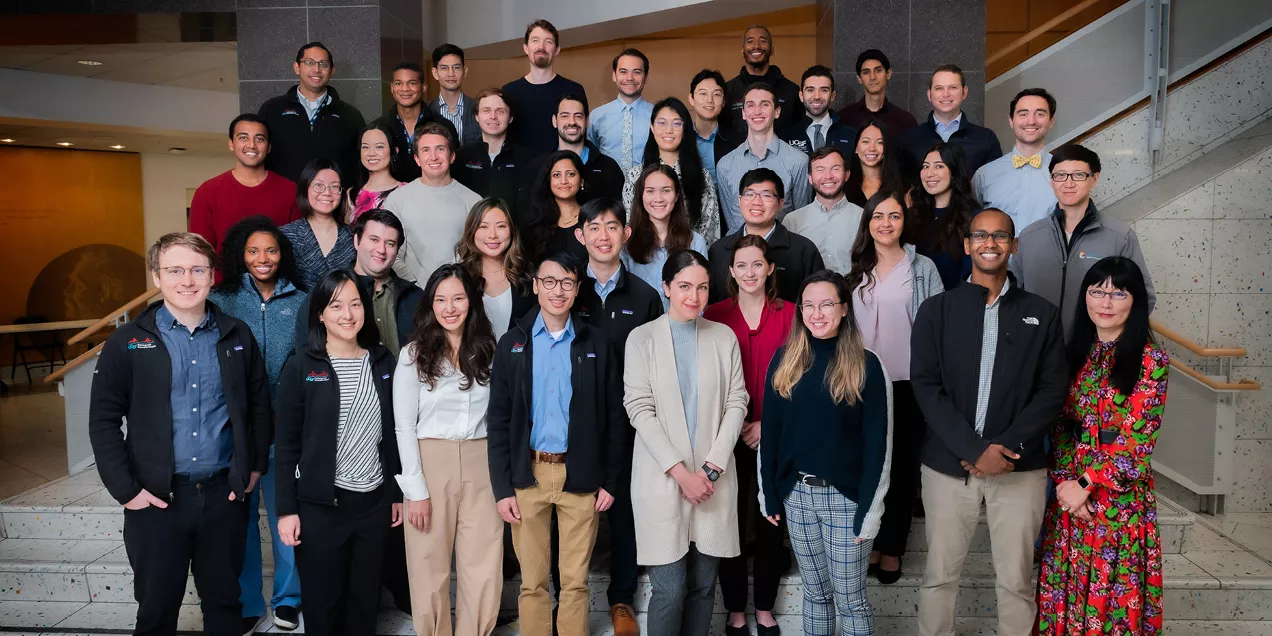 Group portrait of radiology residents, fellows, and faculty gathered on a staircase inside a medical center. The group is dressed in a mix of professional and business-casual attire and poses together in a bright atrium, highlighting the collaborative training environment within the radiology program.