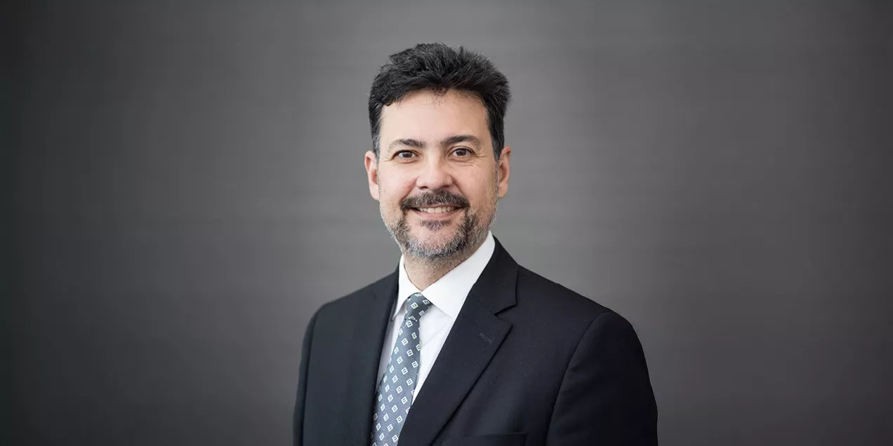 Christopher Hess, MD, PhD, wearing a dark suit and patterned tie, smiles at the camera in a professional portrait against a gray background.