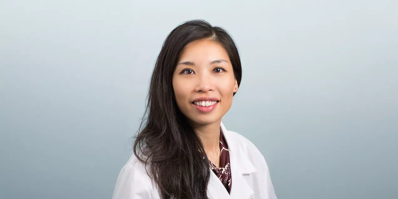 Shirley Chou, MD, wearing a white lab coat, smiles at the camera in a professional portrait against a light blue background.