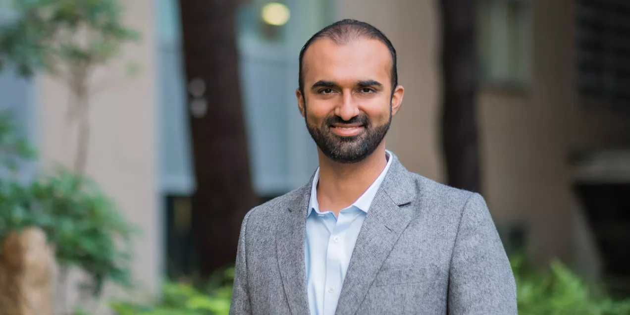 Portrait of Kazim Narsinh smiling outdoors while wearing a gray blazer and light blue dress shirt.