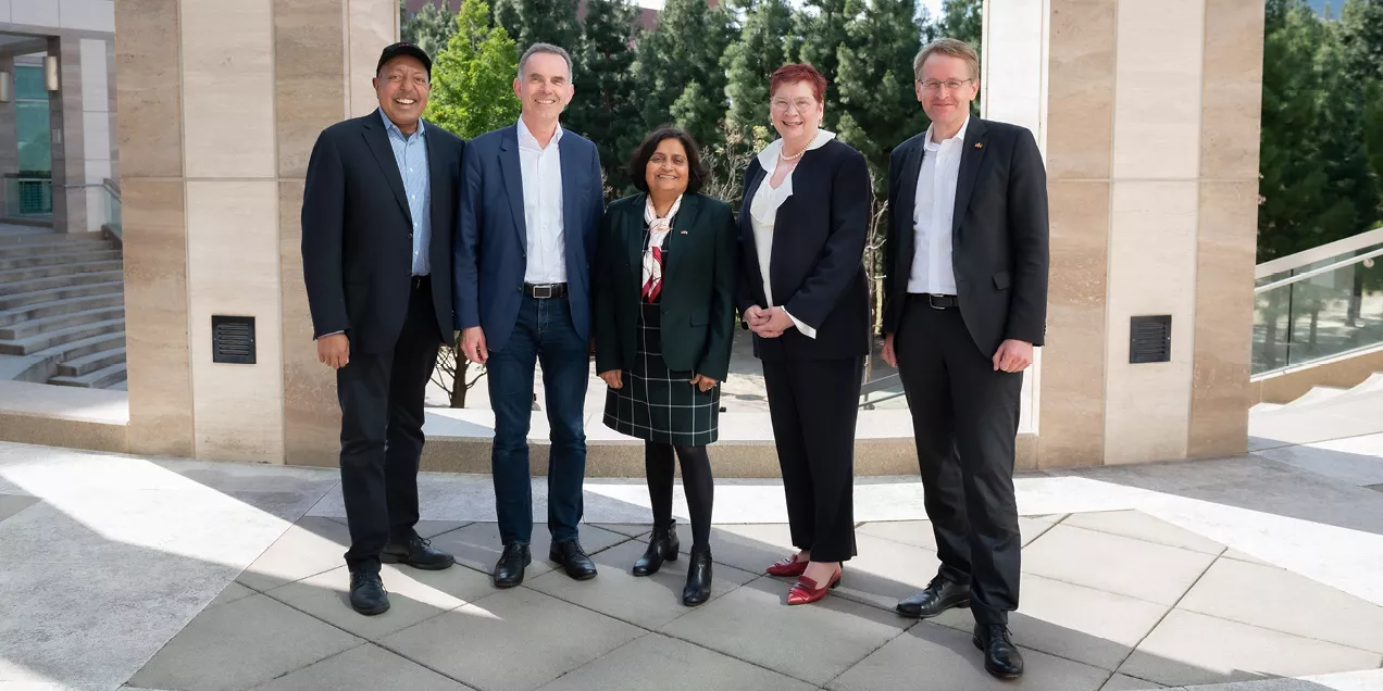 Five professionally dressed individuals stand together outdoors between stone columns, smiling at the camera during the AI Exchange 2024 event.