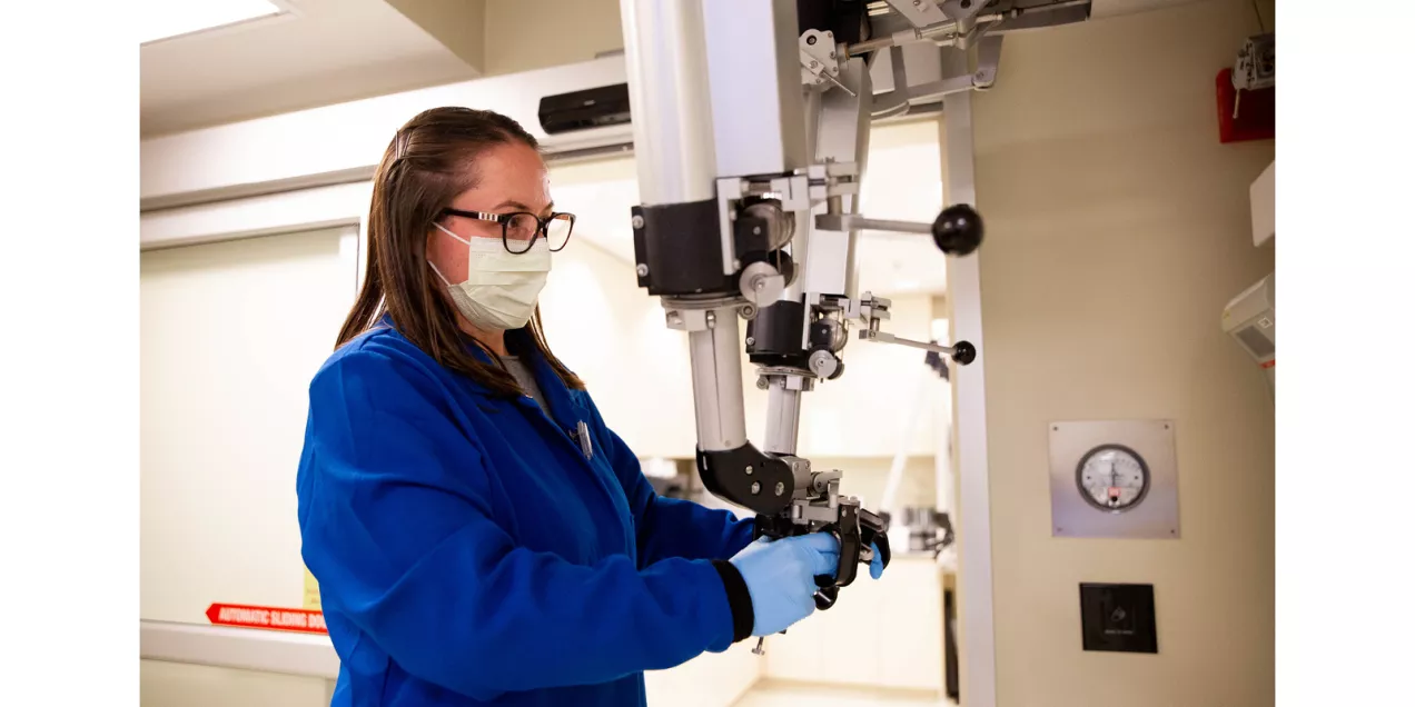 A researcher wearing protective clothing, gloves and a face mask operates laboratory imaging equipment.