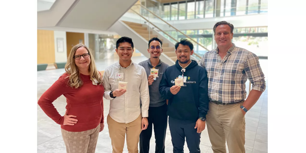 Five staff members pose in a bright hospital lobby, with several holding UCSF MRI safety cookies.