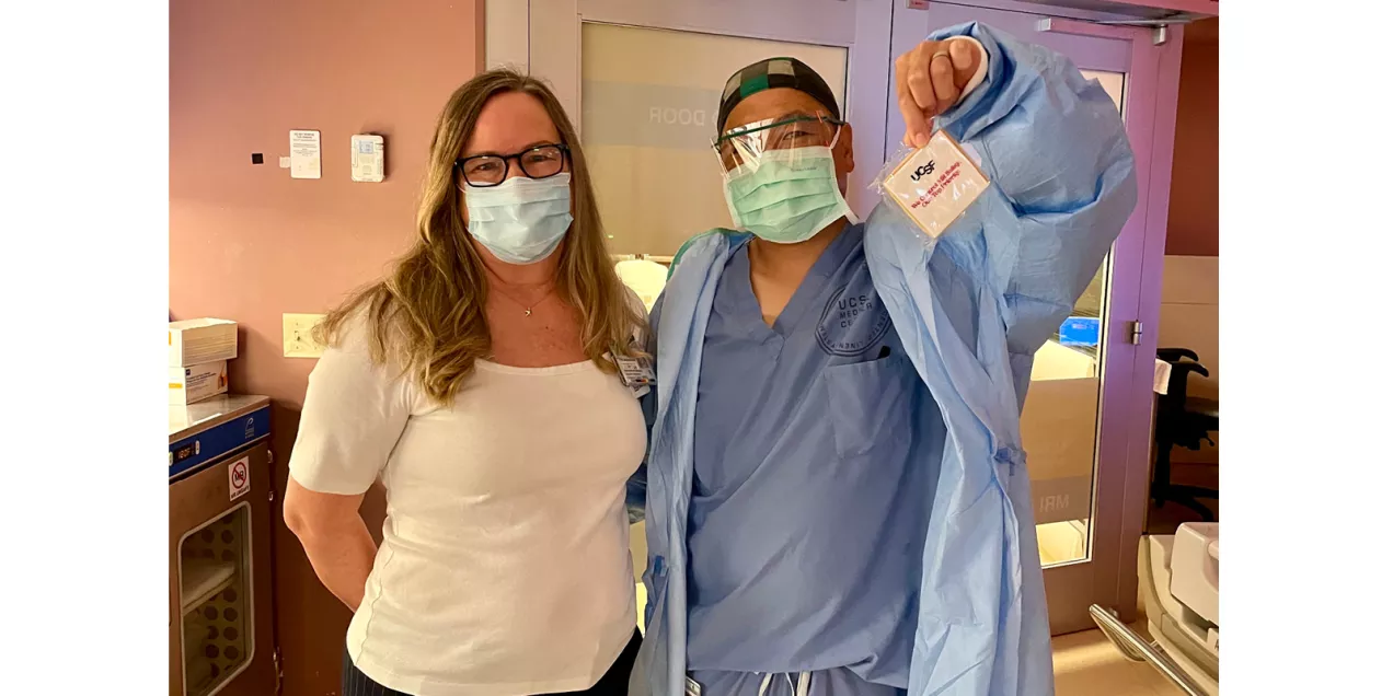 Two masked healthcare staff members pose in a clinical area while one holds up a UCSF MRI Safety Week cookie.