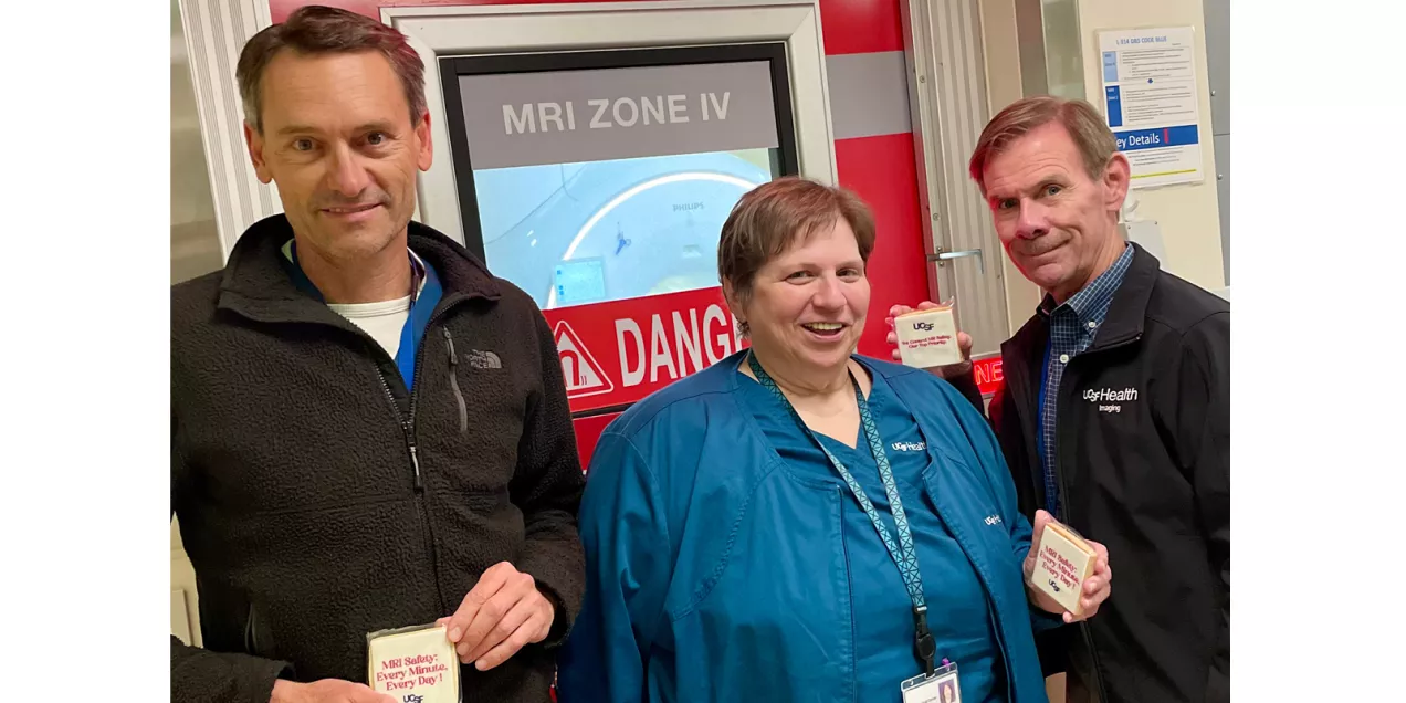 Three healthcare staff members pose in front of an MRI Zone IV entrance while holding UCSF MRI safety cookies.