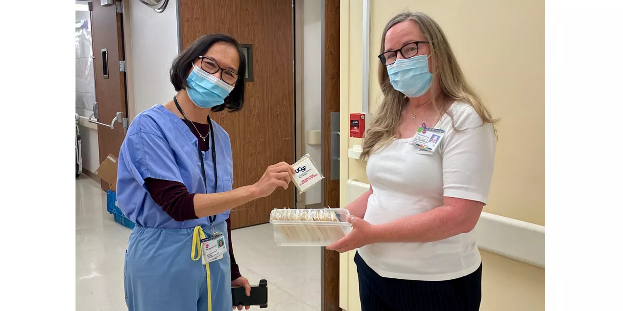 Two masked healthcare staff members in a hospital hallway distribute UCSF MRI Safety Week cookies from a tray.