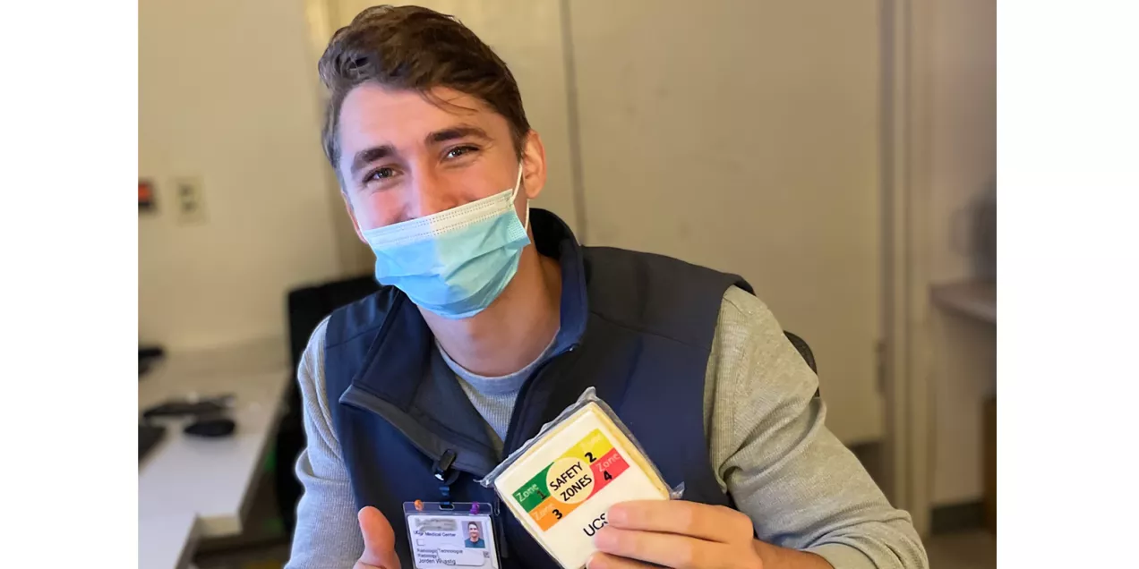 A masked healthcare worker holds up a UCSF cookie illustrating the four MRI safety zones.