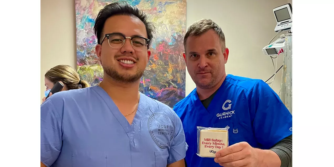 Two healthcare professionals in scrubs pose in a clinical room while displaying a UCSF MRI Safety Week cookie.