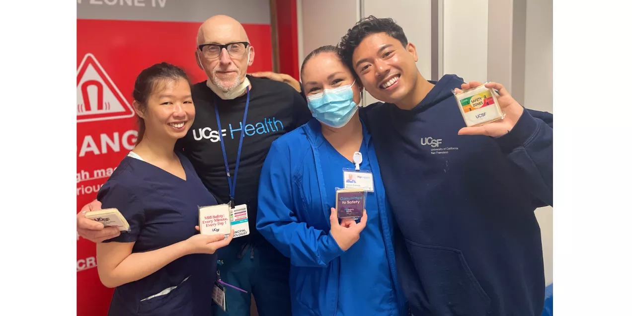Four UCSF healthcare staff members pose near an MRI Zone IV entrance while displaying MRI safety cookies and materials.