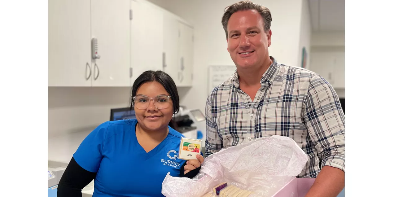 Two people pose with a box of treats while one holds a UCSF MRI safety zones cookie.