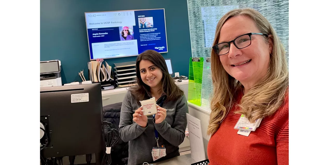 Two UCSF staff members smile at a radiology reception desk while one displays an MRI safety cookie.
