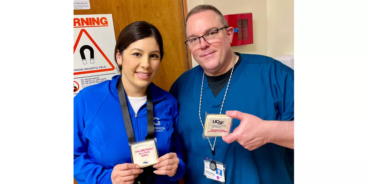 Two healthcare staff members pose in front of an MRI warning sign while holding UCSF MRI Safety Week cookies.