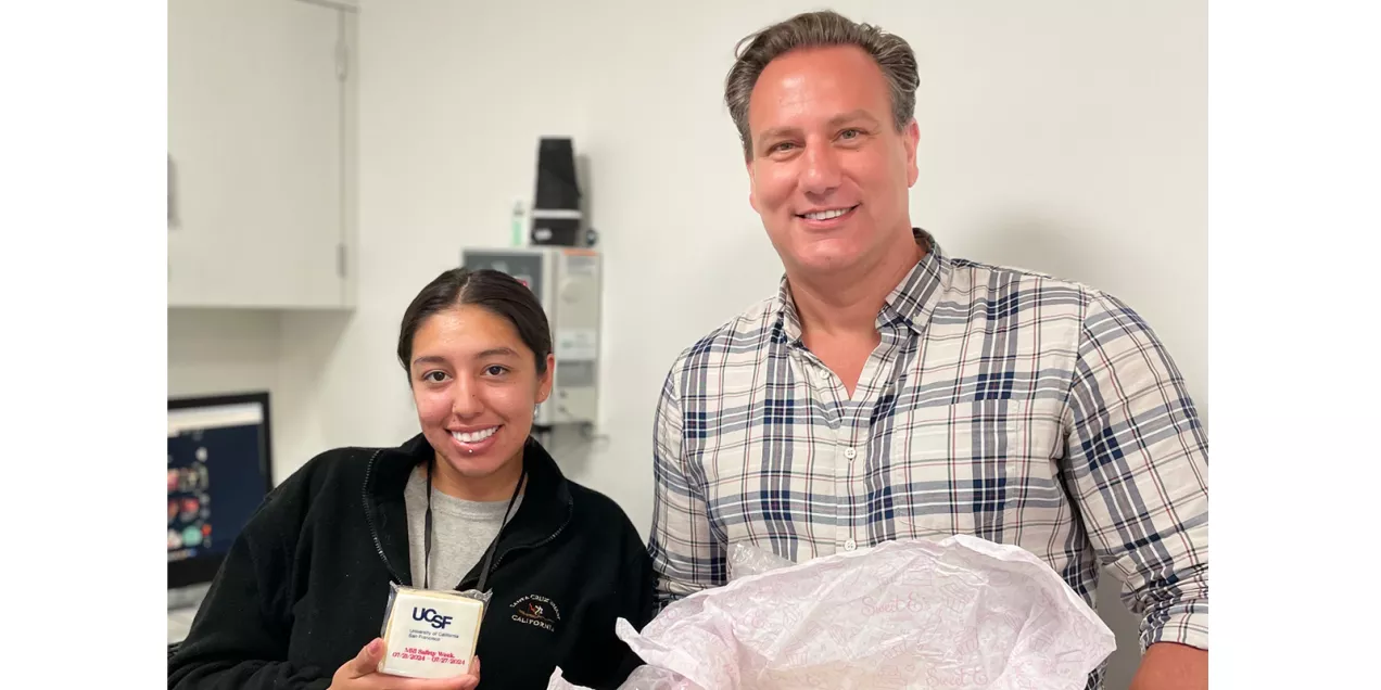 Two staff members pose with an open box of treats while one displays a UCSF MRI Safety Week cookie.