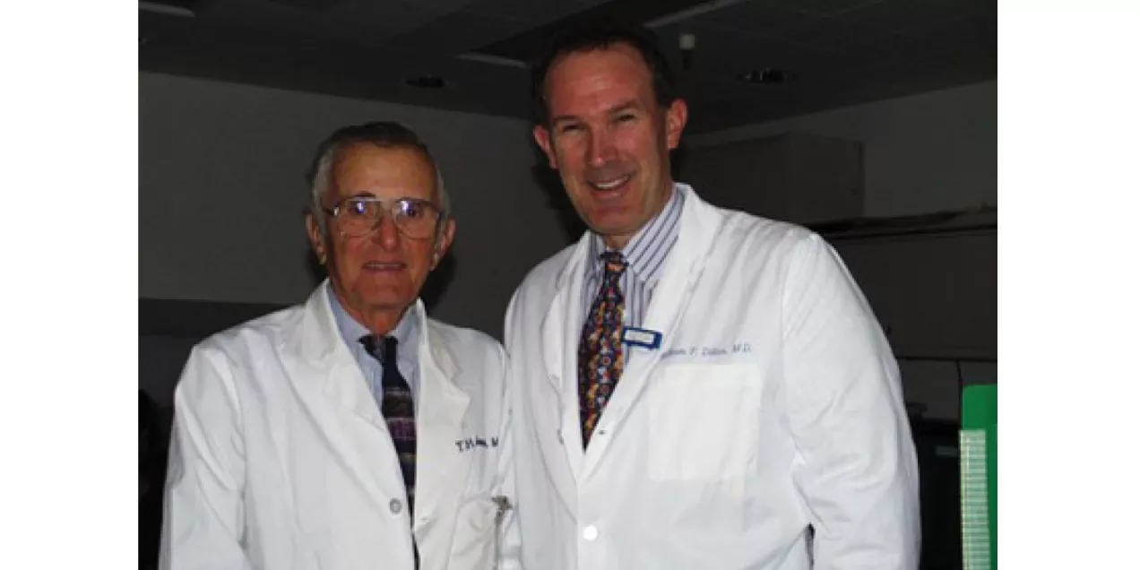 Two physicians wearing white coats standing together and smiling in a clinical setting.