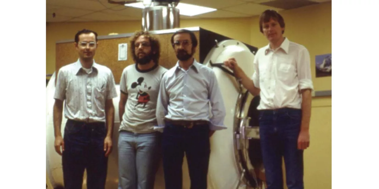 Four men standing together beside an early medical imaging scanner.