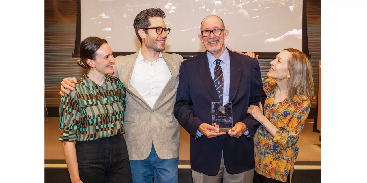 Four people gathered around an award recipient holding a commemorative plaque at a department event.