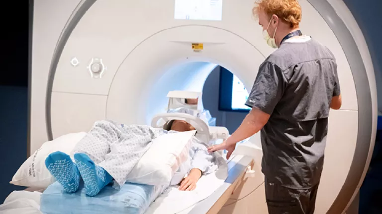 A technologist prepares a patient on the exam table before an MRI scan, adjusting their position as the patient lies ready to enter the scanner.