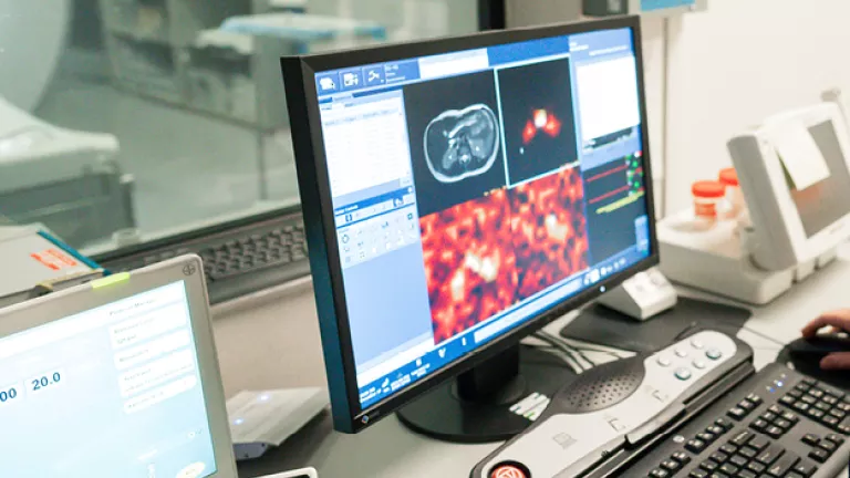 A radiology workstation showing MRI scan images on a computer monitor inside a clinical imaging control room.