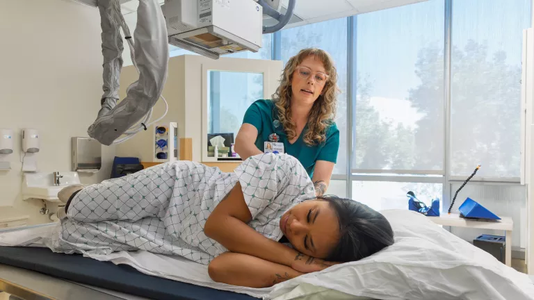 A clinician and a patient interact in a clinical exam room at the Orthopedic Institute, with medical equipment visible nearby.