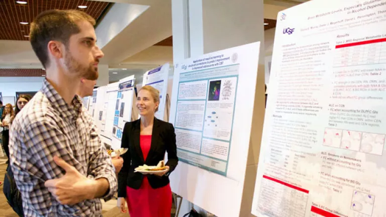 Attendees stand and discuss research posters during a scientific poster session, with UCSF posters displayed on easels in a conference space.