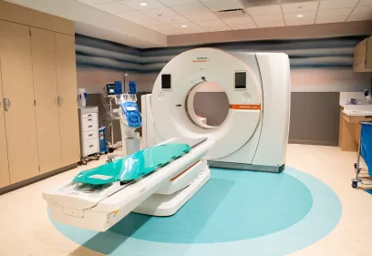 A CT scan room featuring a Siemens SOMATOM X.cite scanner with the patient table extended, surrounded by medical equipment and storage cabinets in a clean, modern clinical setting.