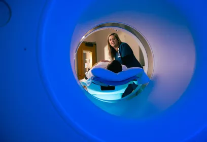 Radiologic technologist positioning a patient on a CT scanner table, viewed from inside the scanner ring.