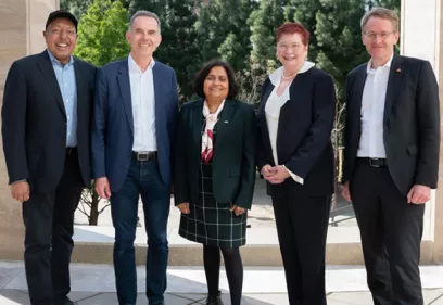 Five professionally dressed individuals stand together outdoors between stone columns, smiling at the camera during the AI Exchange 2024 event.