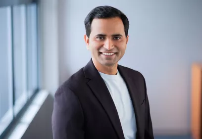 Professional portrait of Anil Bidkar, PhD, smiling and standing indoors near a window while wearing a dark blazer over a light-colored shirt.
