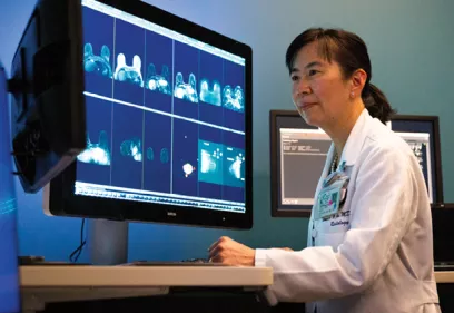 A radiologist reviews breast imaging scans displayed on a large medical monitor in a clinical reading room. Multiple breast MRI images are visible on the screen as she analyzes the results, highlighting the role of advanced imaging in breast cancer detection and diagnosis.