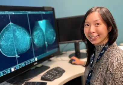 Healthcare professional seated at a workstation reviewing mammogram images displayed on a computer monitor in a breast imaging reading room.