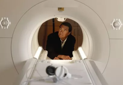 Michael Weiner peers inside an MRI scanner, highlighting his pioneering role in advancing medical imaging and Alzheimer's disease research. The image shows him examining the scanner from within the bore, emphasizing his decades of innovation in neuroimaging.