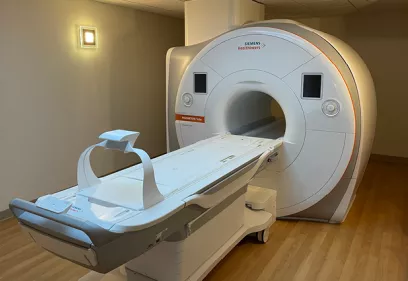 A Siemens Healthineers MRI scanner in a clinical imaging suite with the patient table extended, wood flooring, and soft ambient lighting.